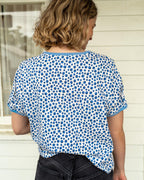 Women facing away wearing a blueberry printed tee against a white wall. 