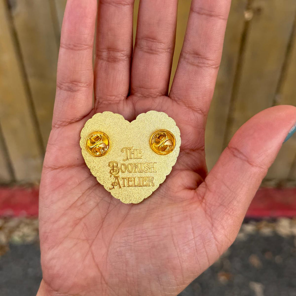 Heart-shaped gold pin with 'The Bourish Atelier' branding held in a hand.