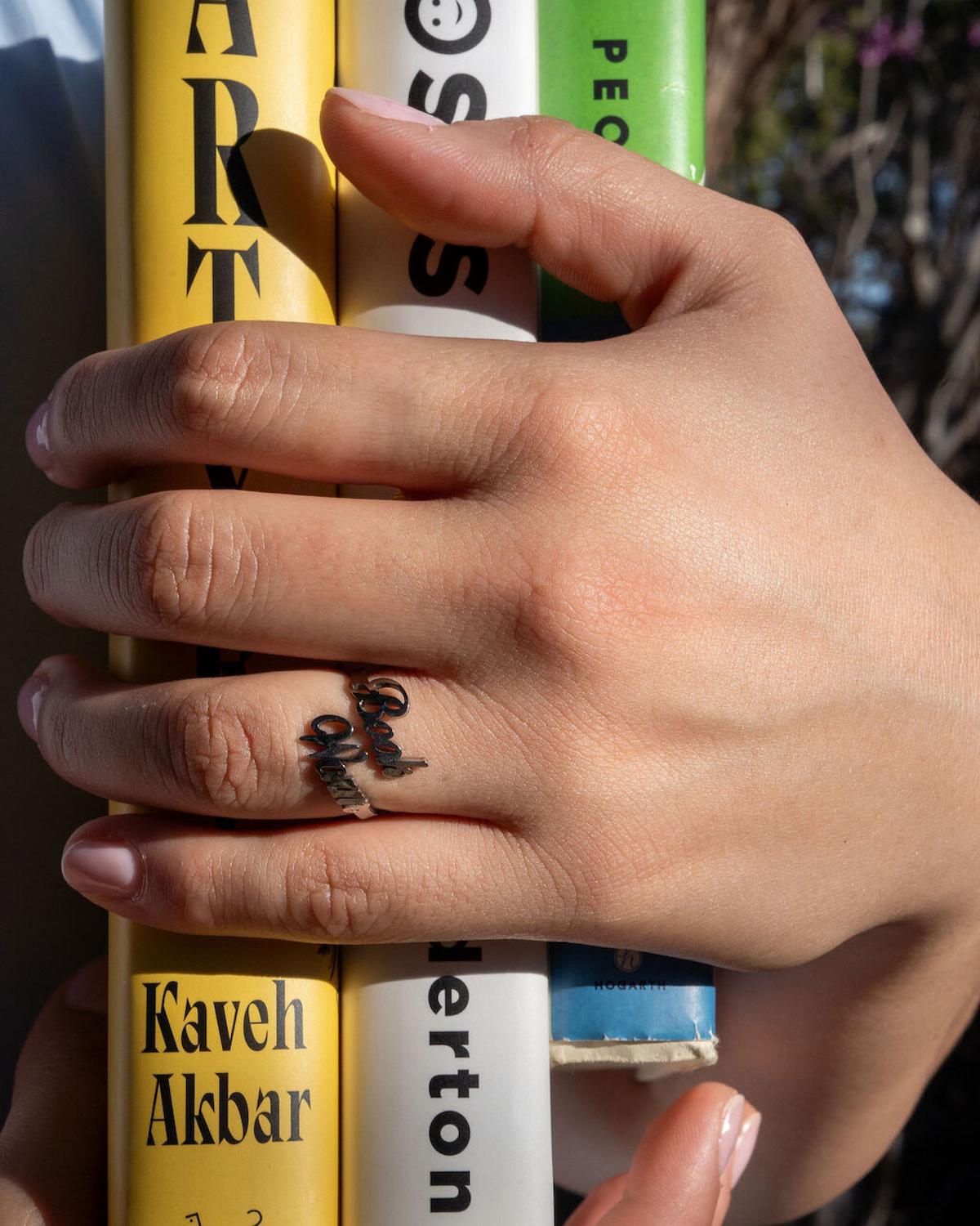 Hand holding three cans of Kaveh Akbar, Pecos, and another brand against a blurred background.