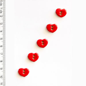 Red heart-shaped buttons on a white background with a ruler for scale.