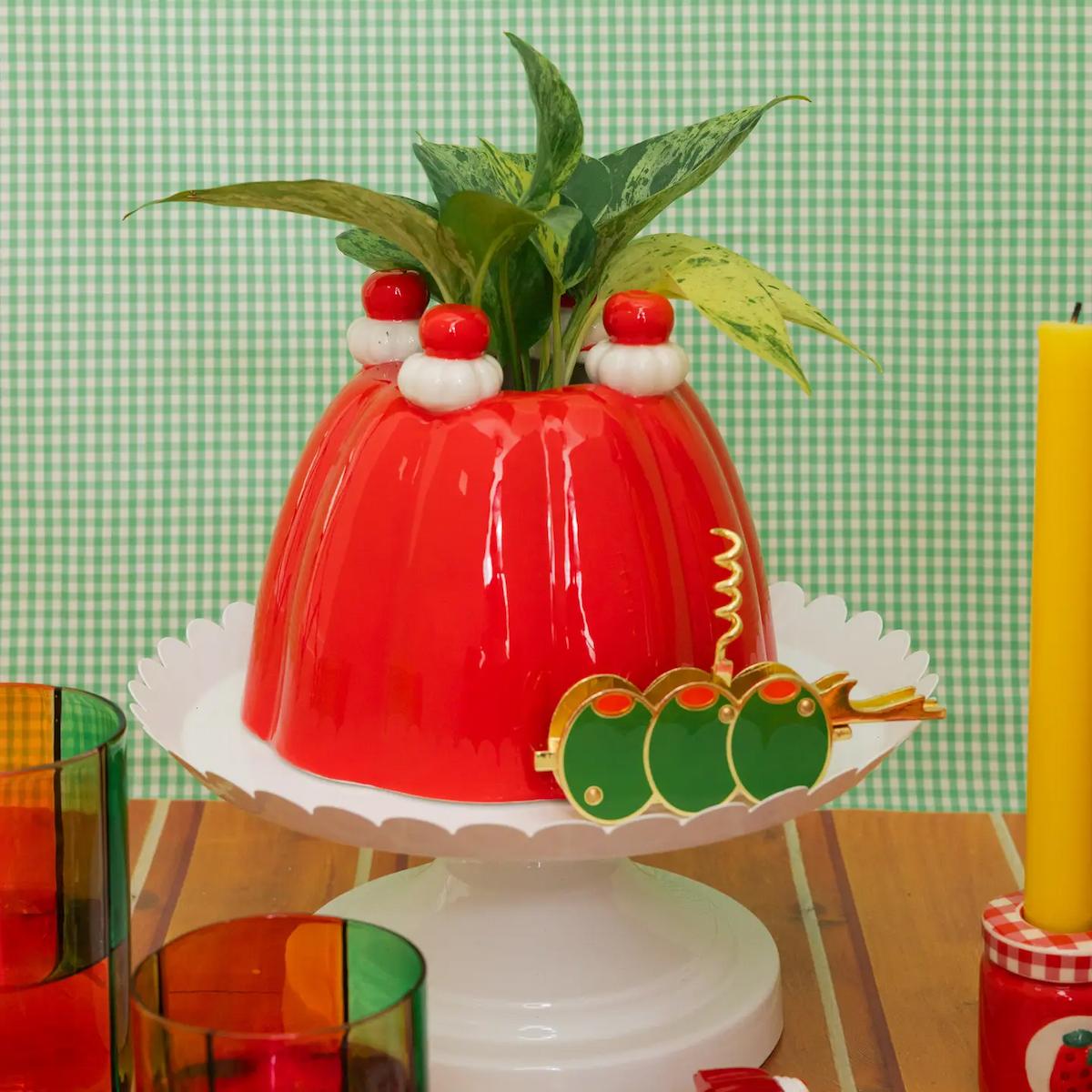 Red gelatin mold with green leaves on a white stand against a green checkered background
