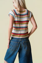 Person wearing a colorful crochet top and blue jeans against a beige background