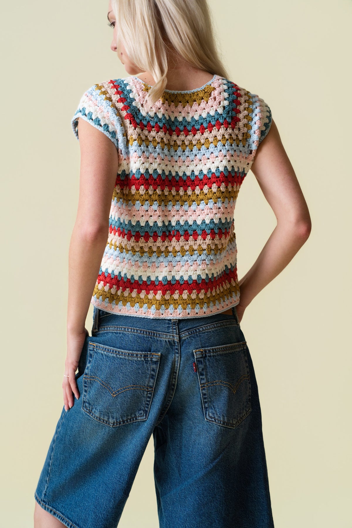 Person wearing a colorful crochet top and blue jeans against a beige background