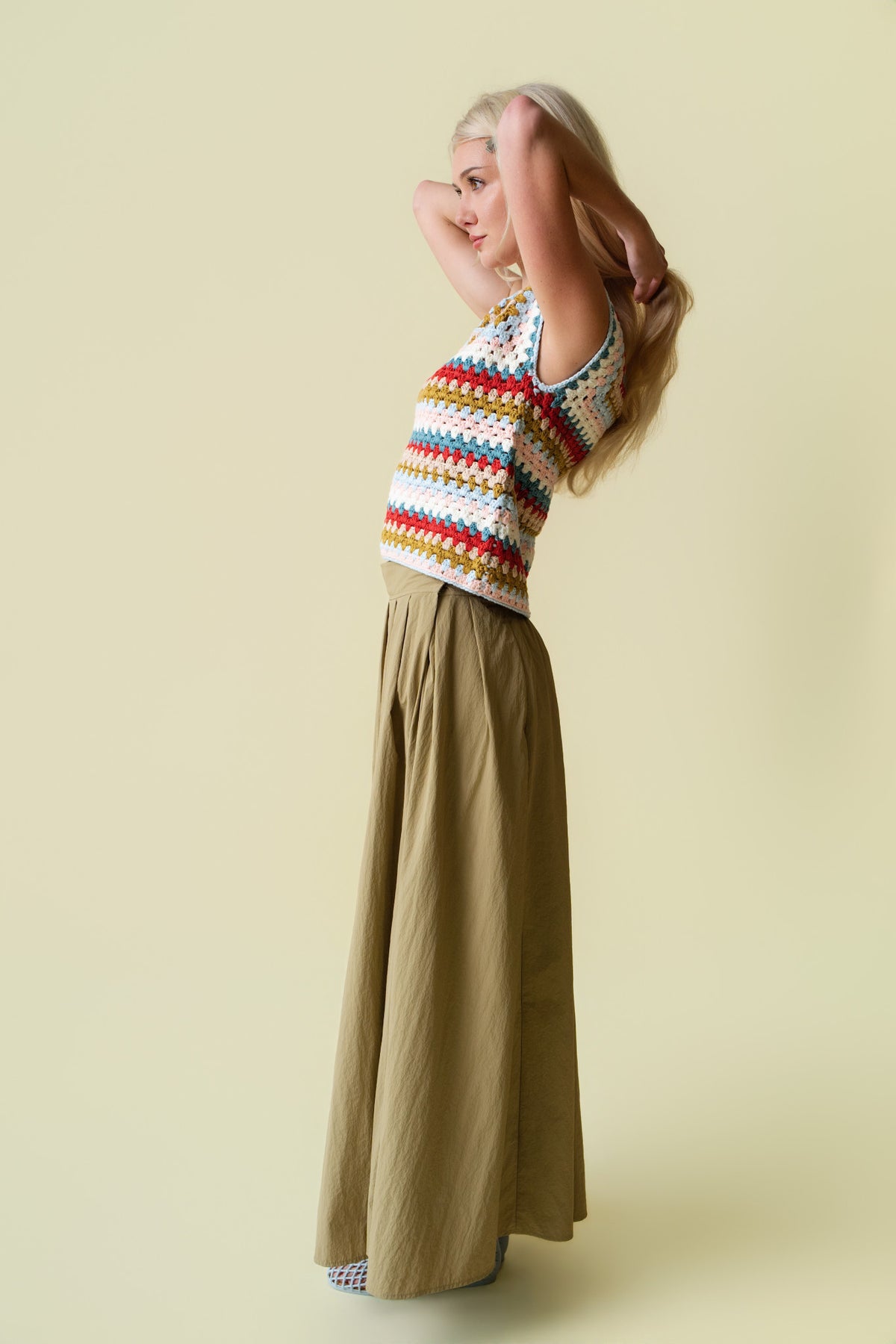 Person wearing a colorful crochet top and green skirt on a beige background