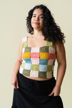 Person wearing a colorful crocheted tank top against a beige background