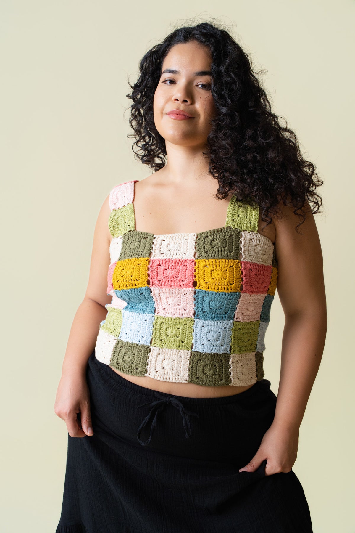 Person wearing a colorful crocheted tank top against a beige background