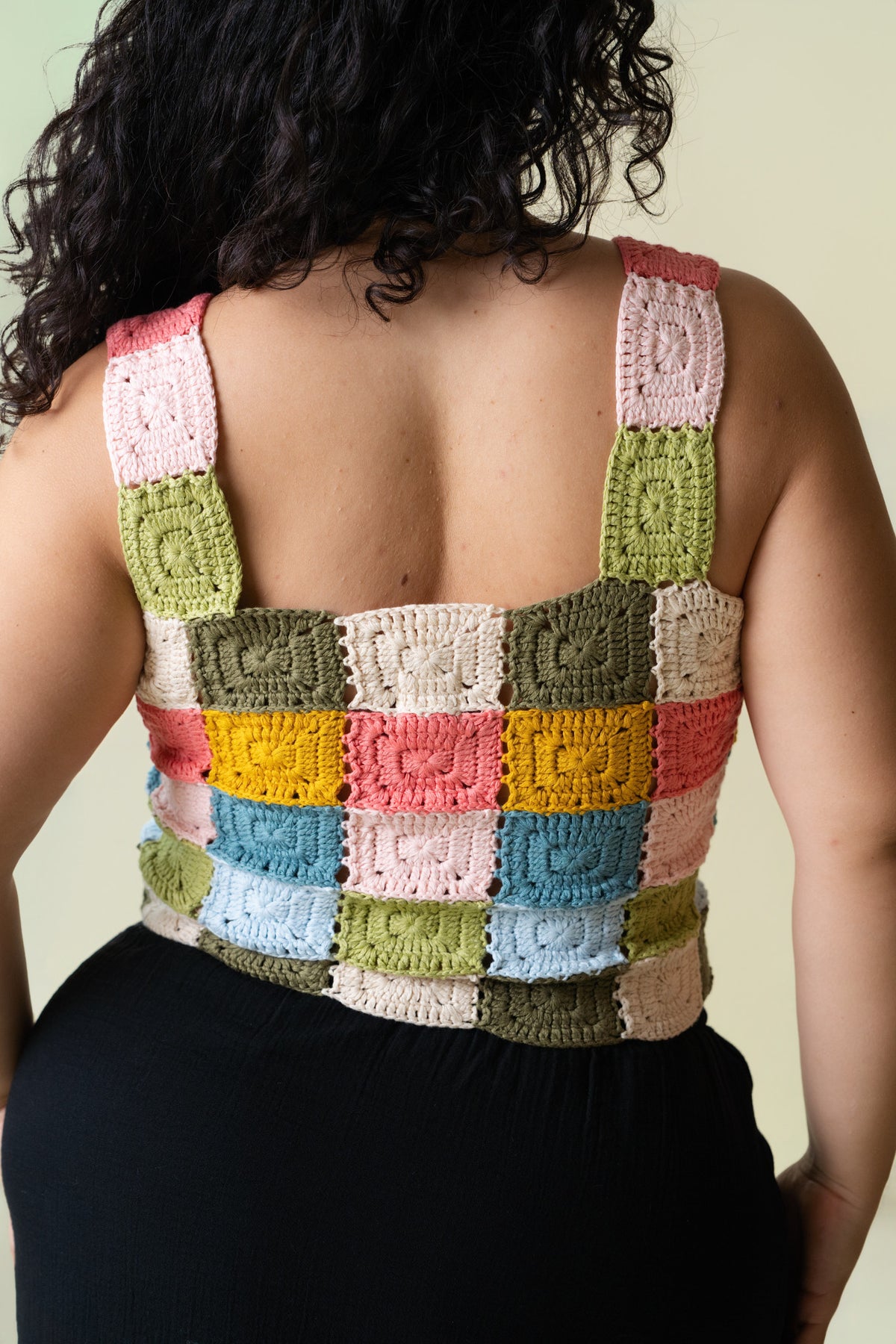 Back of person wearing a colorful crocheted tank top against a beige background