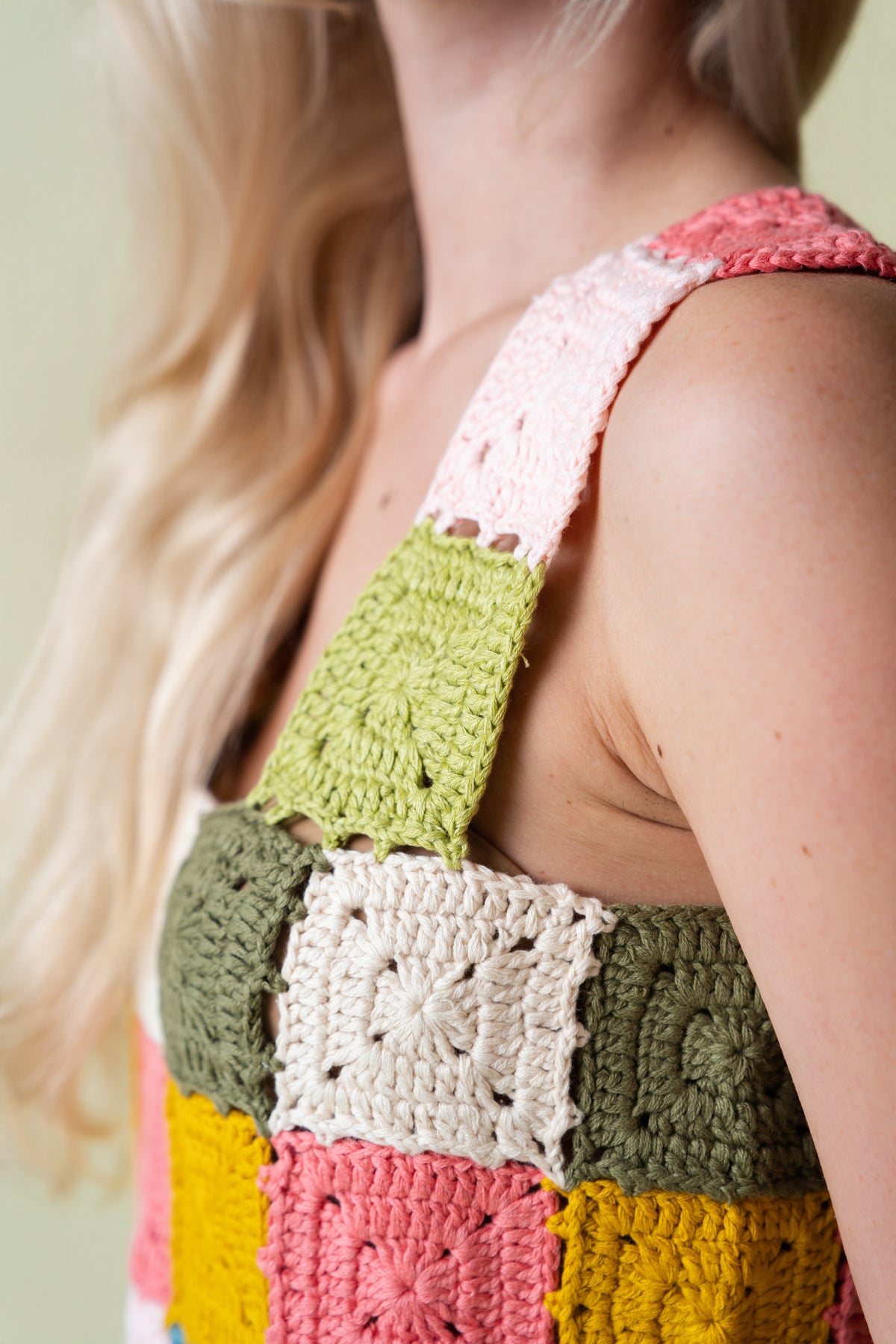Side of person wearing a colorful crochet patterned top on a beige background