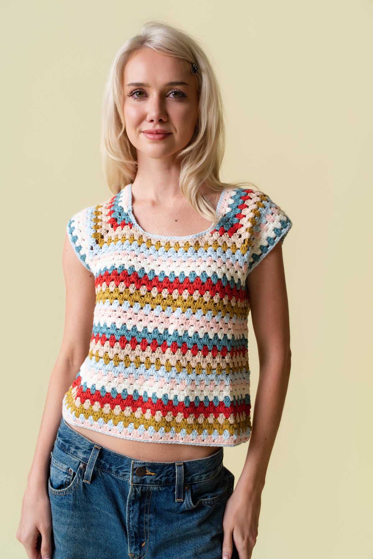 Person wearing a colorful crochet top and jeans against a beige background