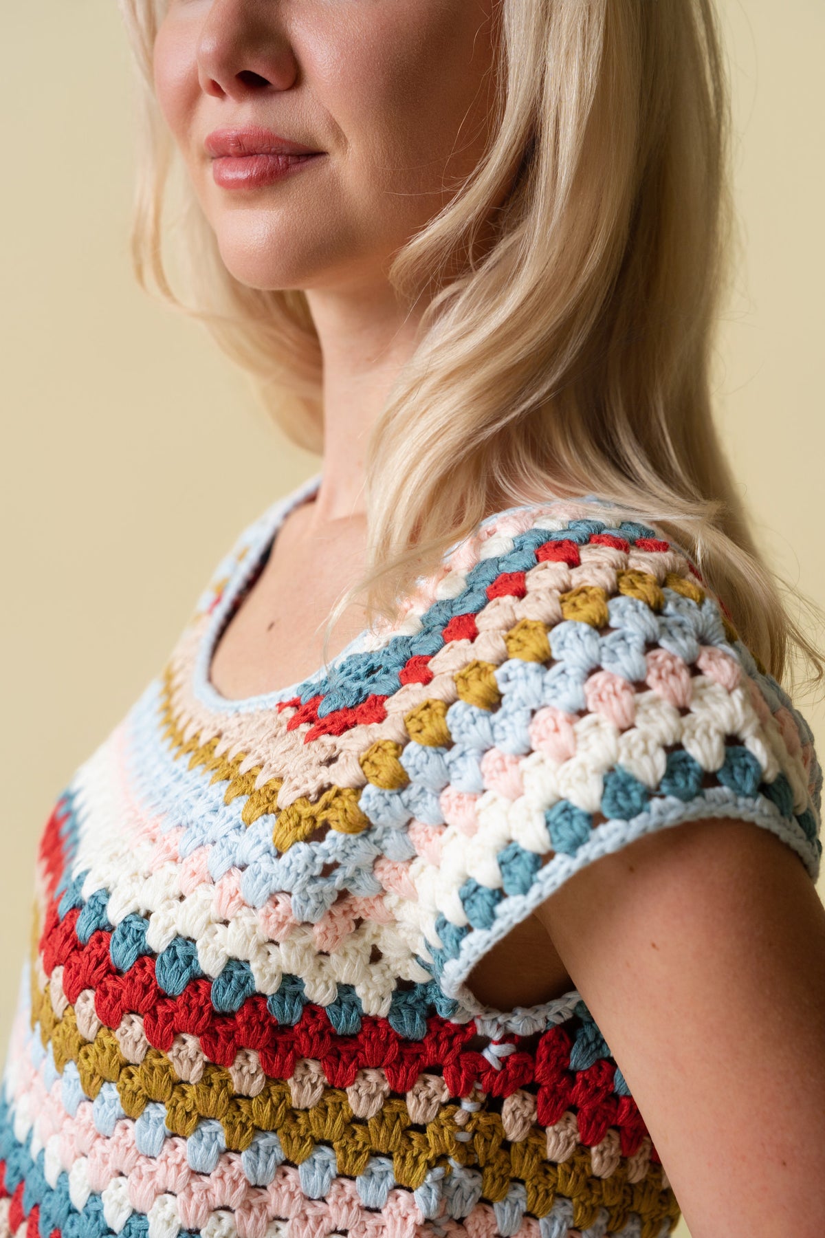 Person wearing a colorful crochet top against a beige background