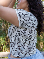 Person wearing a black and white geometric patterned top with a blurred natural background