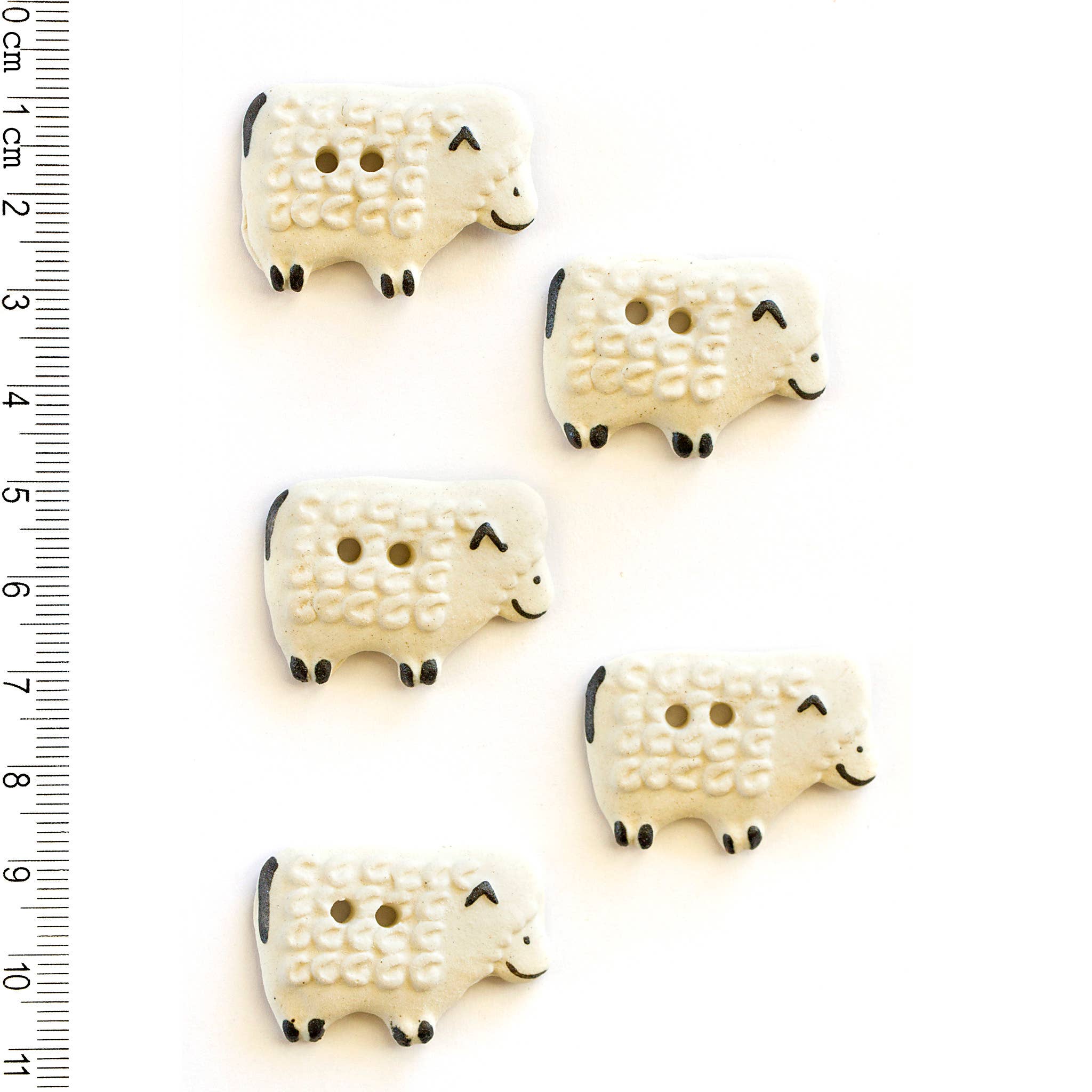 Five white sheep-shaped buttons with black details on a white background, accompanied by a ruler for scale.