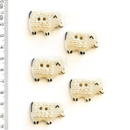 Five white sheep-shaped buttons with black details on a white background, accompanied by a ruler for scale.