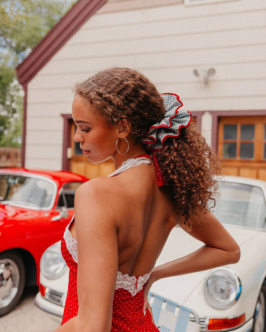 A woman wearing a red and blue hair scrunchie standing outdoors in front of classic cars.