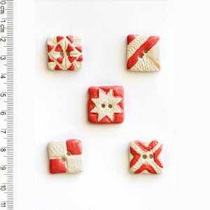 Five decorative buttons with red and white patterns on a white background, accompanied by a ruler for scale.