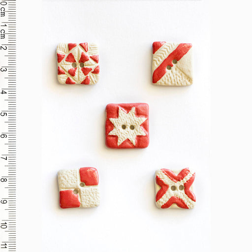 Five decorative buttons with red and white patterns on a white background, accompanied by a ruler for scale.