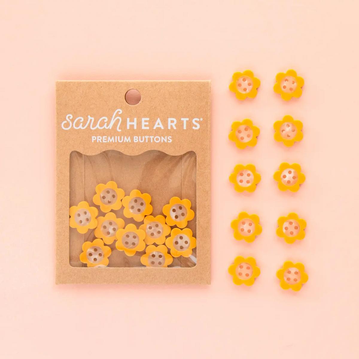 Packaged yellow flower buttons with 'sarah HEARTS' branding on a pink background