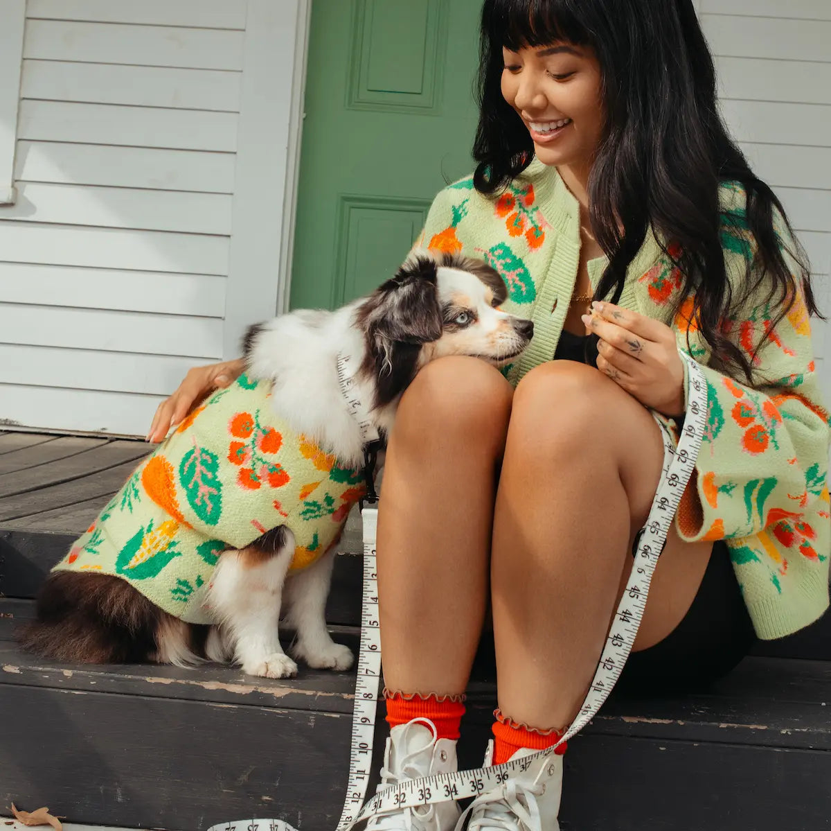 Woman in a veggie print sweater sitting on a step with a dog, both wearing matching outfits.