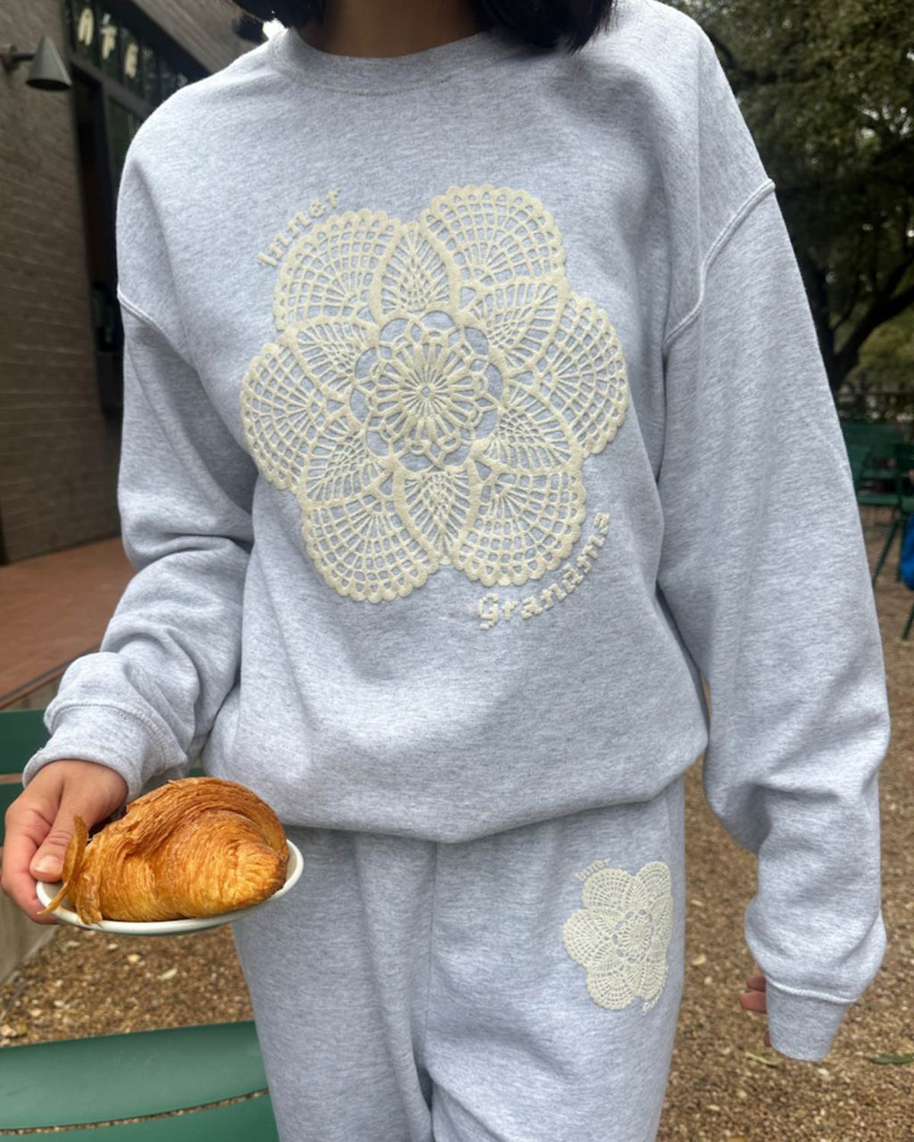 Person wearing a gray sweatshirt with lace design, holding a pastry.