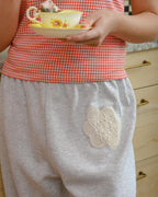 Person wearing a red checkered top and gray pants with a lace patch, holding a small dish.