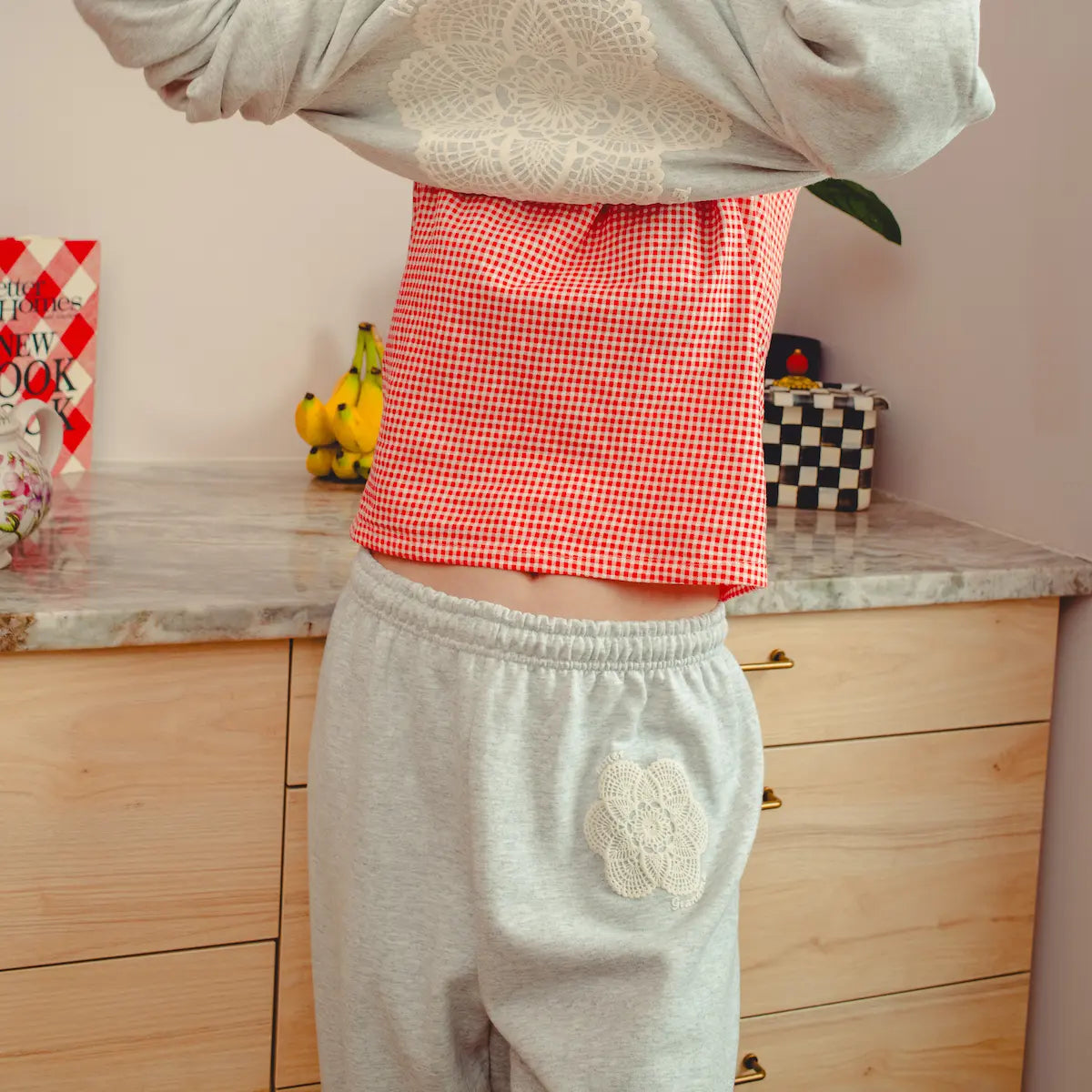 Person wearing a red checkered top and doily printed gray sweatpants in a kitchen setting.