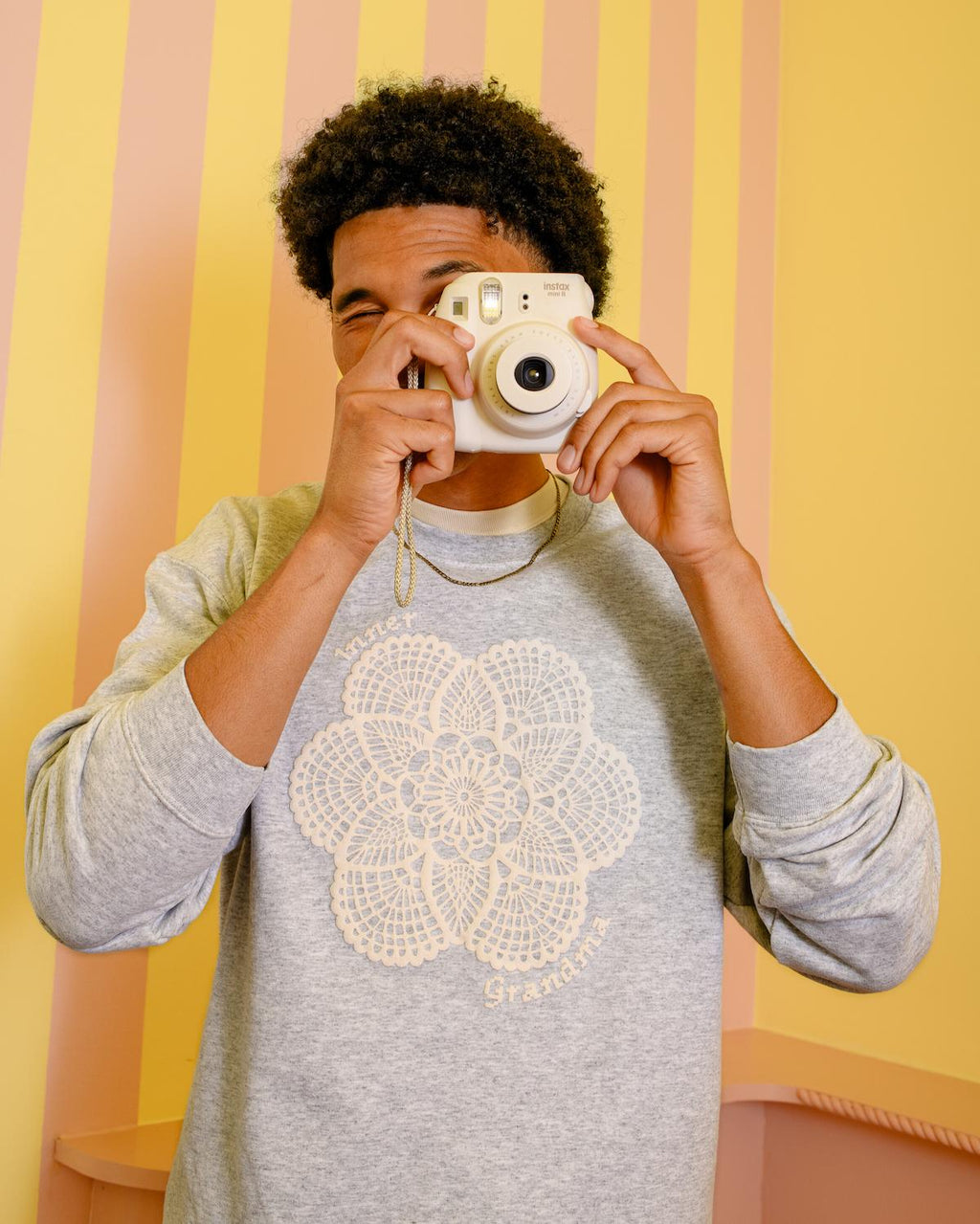 Person holding a camera against a striped yellow and pink background