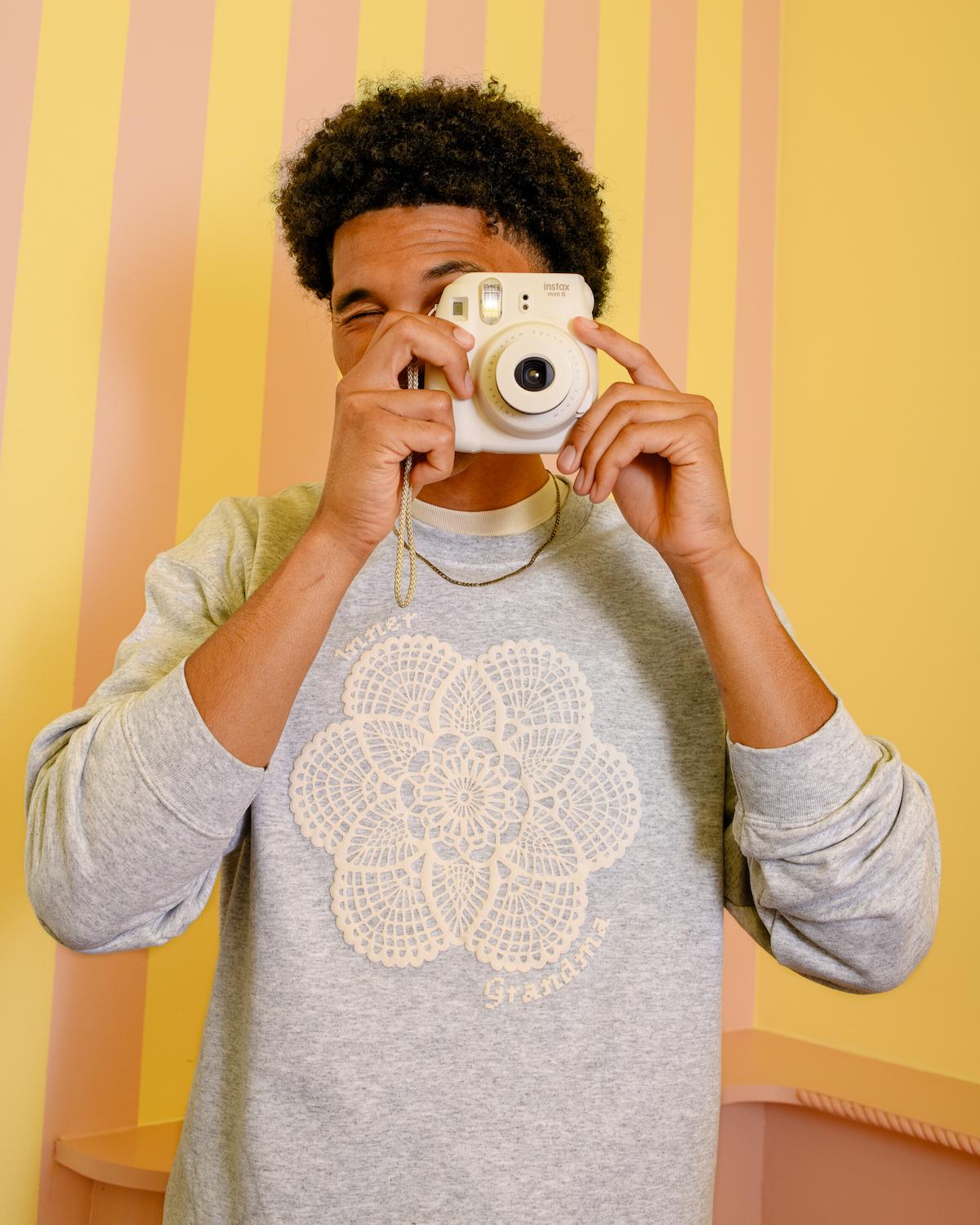 Person holding a camera against a striped yellow and pink background