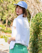 Woman wearing a light gray shirt with a floral design and a green checkered skirt outdoors.
