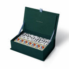 Open green box containing a set of dominoes with floral designs on a white background