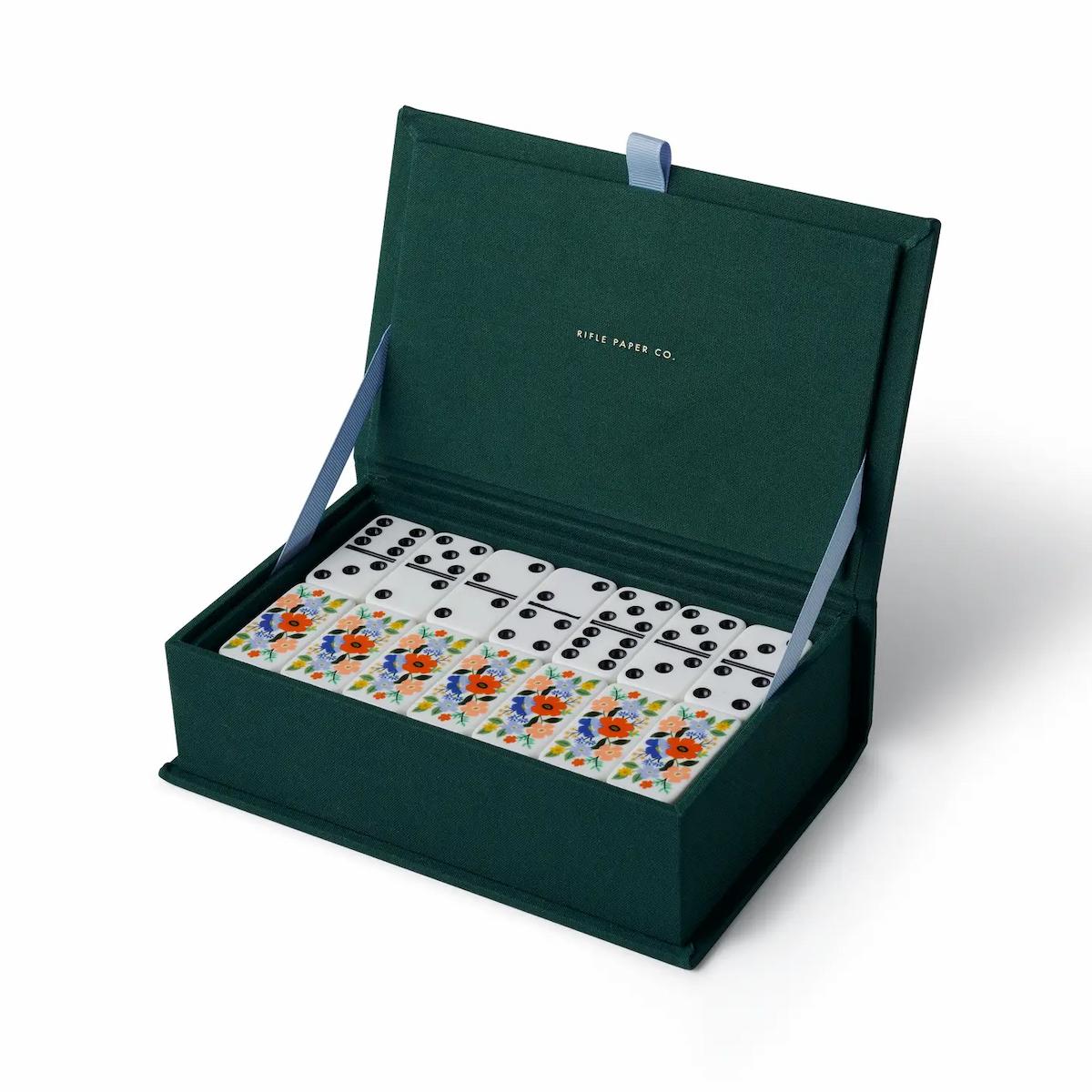 Open green box containing a set of dominoes with floral designs on a white background