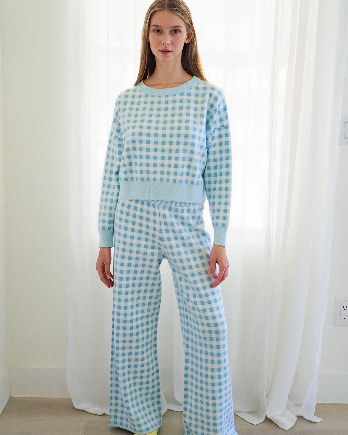 Person standing in a bright room wearing a matching light blue and white gingham two-piece loungewear with yellow socks.