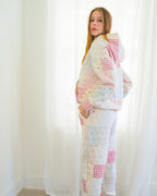 Person standing in a bright room wearing a pastel patchwork quilted hoodie and matching jogger pants with olive green socks.
