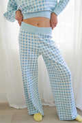 A person wearing a light blue and white gingham knit lounge set standing in front of white curtains.