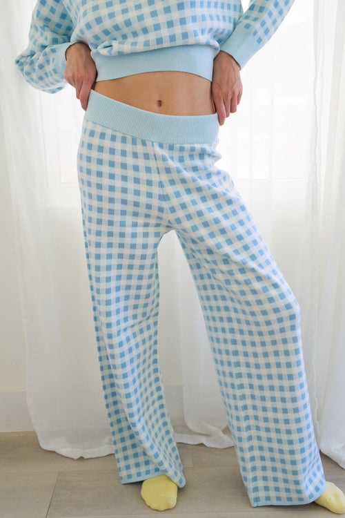 A person wearing a light blue and white gingham knit lounge set standing in front of white curtains.