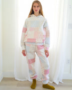 Person standing in a bright room wearing a matching patchwork hoodie and jogger pants set in pastel pink, white, and light blue fabrics, paired with olive green socks.