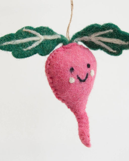 A pink felt radish hanging ornament with green felt leaves and a stitched smiling face, suspended by a thin string against a plain white background.