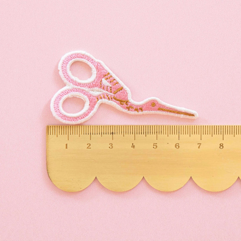 Pink scissors iron on patch with gold accents on a pink background