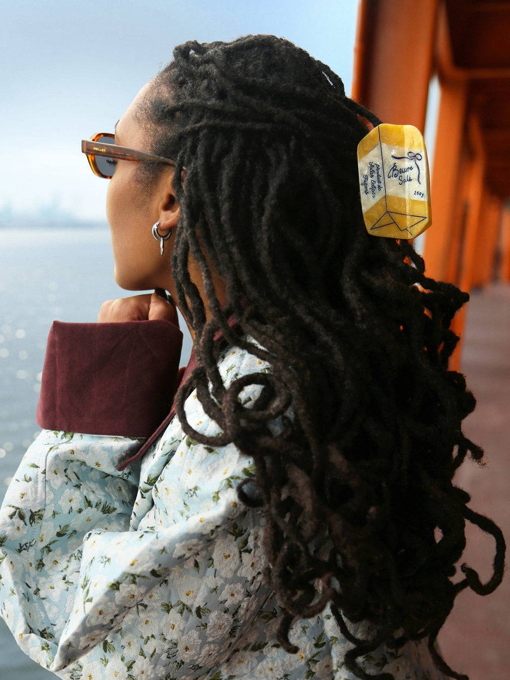 Person with long braided hair looking out over a body of water wearing a yellow butter claw clip