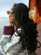 Person with long braided hair looking out over a body of water wearing a yellow butter claw clip