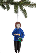 Ornament of Ina Garten in a blue coat holding a spoon and a bowl, hanging from a Christmas tree.