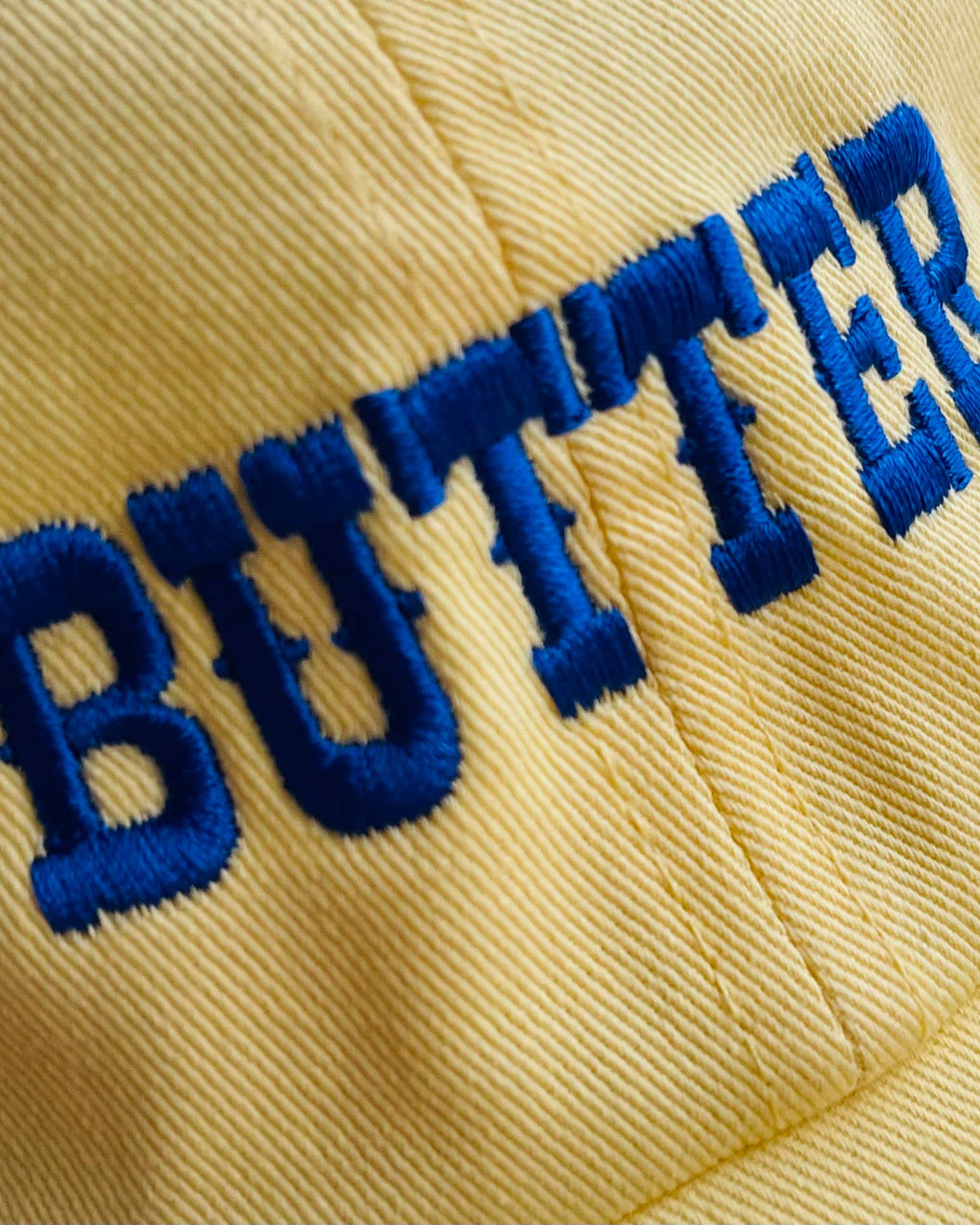 Close-up of a yellow cap with 'BUTTER' embroidered in blue thread.