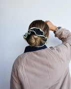 Person wearing a patterned black and white scrunchie with a plain background