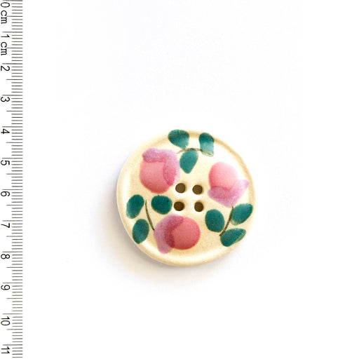 Off-white floral button with pink flowers and green leaves on a white background, next to a ruler for scale.