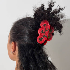 Person wearing a red tomato hair claw clip on a plain background