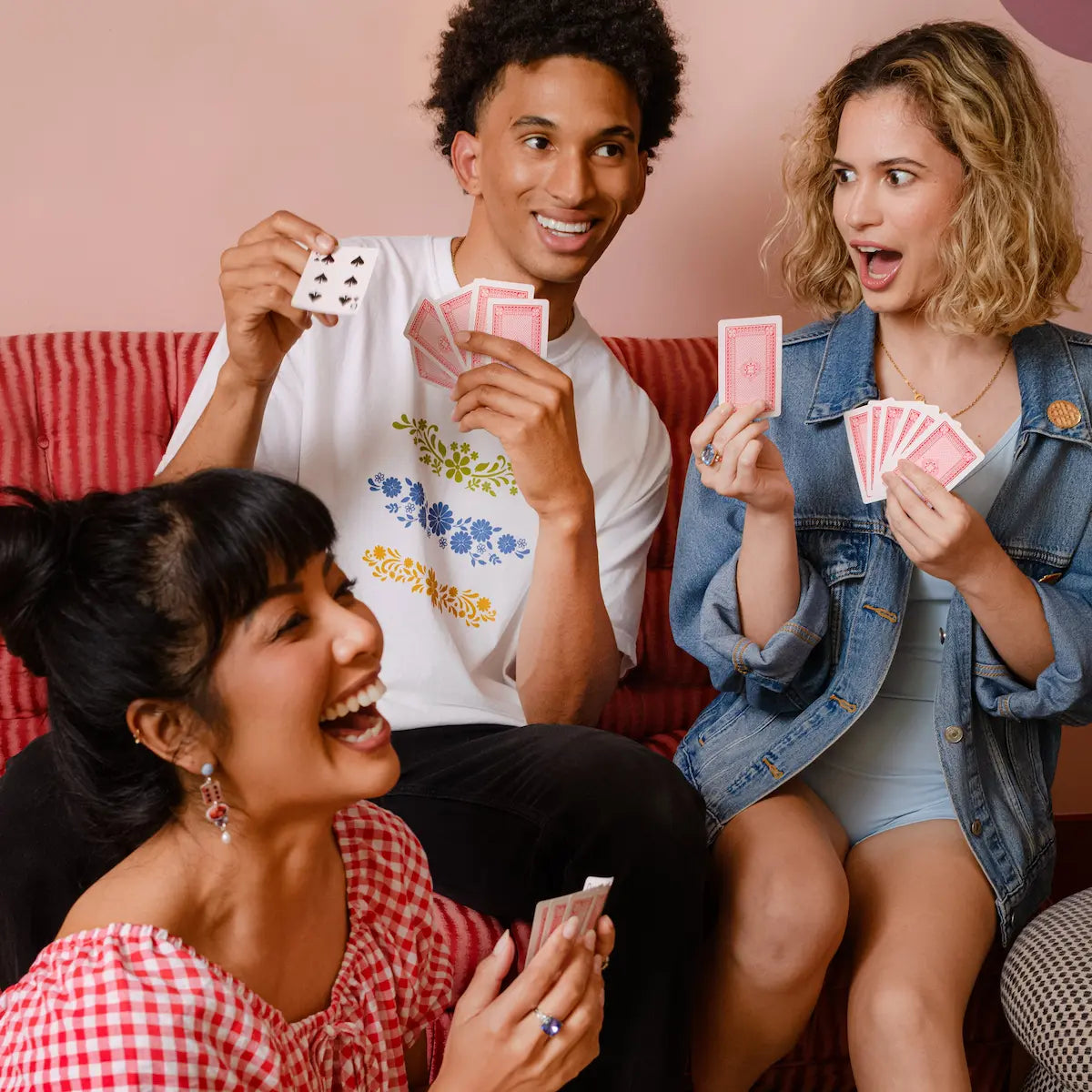 Three friends playing cards together on a couch with confetti on the floor.