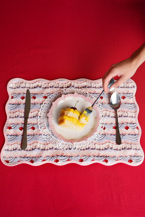 Dessert plate with slice of cake on a frosting patterned place mat against a red background