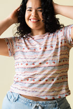 Person wearing a pink and purple frosting patterned shirt with cherries on it and light blue jeans against a beige 