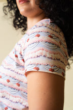 Side of a person wearing a pink and purple frosting patterned shirt with cherries on it