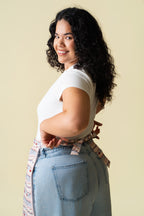 Person wearing a white t-shirt and light blue jeans with a frosting patterned apron against a beige background