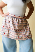 Person wearing a frosting patterned apron over a white shirt and blue jeans on a beige background.
